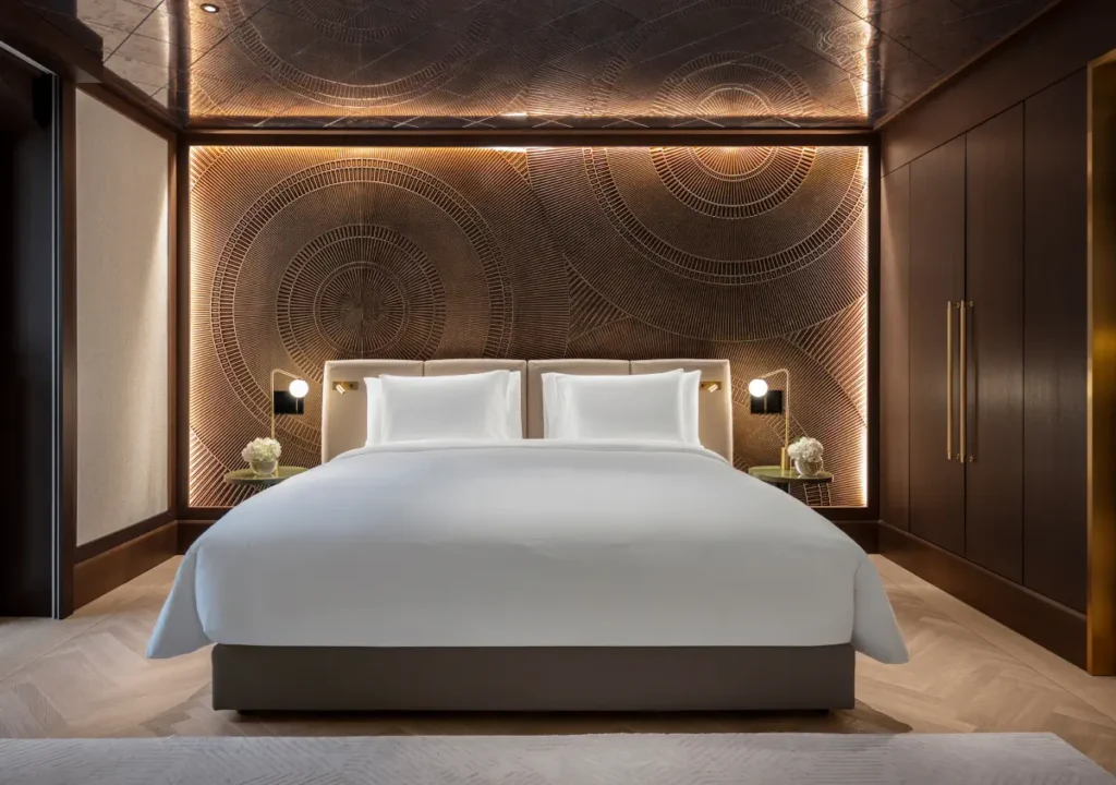 Ein modernes Hotelzimmer im Almanac Palais Vienna verfügt über ein großes Bett mit weißer Bettwäsche, eine dunkle Holzvertäfelung, dekorative Wandkunst, Nachttische und eine sanfte Raumbeleuchtung.